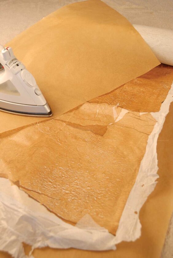 Place beige bag pieces over white plastic fabric. The beige plastic should overlap randomly in places. Iron and fuse as before. Don’t worry if beige plastic skips a spot, folds or creases on itself—this will add character. Add more scraps as desired. Hold “fabric” up to the light to see how it will look illuminated.